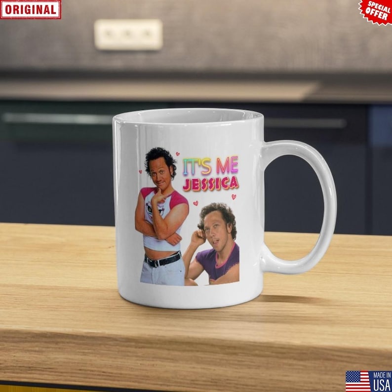 May include: White ceramic mug featuring two images of a man and the text "IT'S ME JESSICA" in colorful letters. The mug has a curved handle and is sitting on a wooden surface.