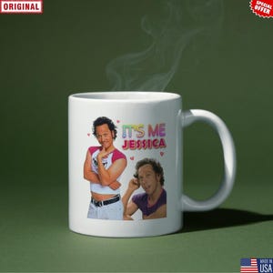 May include: White ceramic mug featuring two images of a man and the text "IT'S ME JESSICA" in colorful letters. The mug has a curved handle and is set against a green background.
