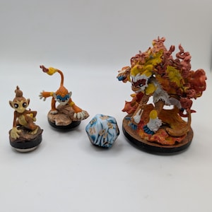 Może przedstawiać: Kolekcja figurek fantasy i wielościennej kostki do gry. Figurki przedstawiają postacie z kreskówek w odcieniach pomarańczu, brązu i żółci. Kostka jest niebiesko-biała ze złotymi numerami. Figurki stoją na okrągłych podstawach.