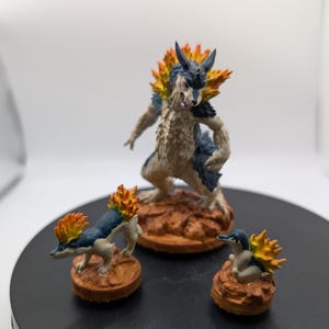 May include: Three painted figurines of a fire-type Pokemon. The largest figurine is a dark blue and white creature with orange flames on its back. The two smaller figurines are smaller versions of the larger figurine.