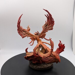 May include: A red and orange phoenix figurine with outstretched wings, standing on a base of flames. The figurine is made of painted resin and is a fantasy creature.