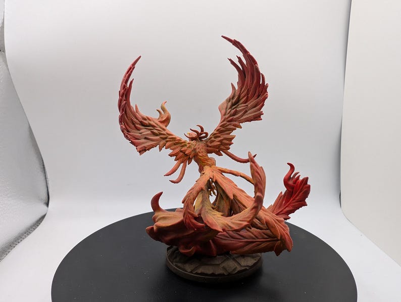 May include: A red and orange phoenix figurine with outstretched wings, standing on a base of flames. The figurine is made of painted resin and is a fantasy creature.
