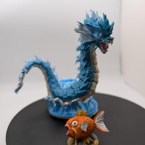 Op de afbeelding: Een blauwe en witte drakenfiguur met een rode mond en een kleiner oranje visfiguur met een gele vin.