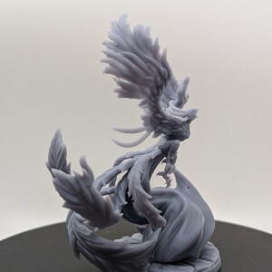 May include: A gray 3D printed miniature of a phoenix with its wings spread wide. The phoenix is perched on a base with a swirling design.