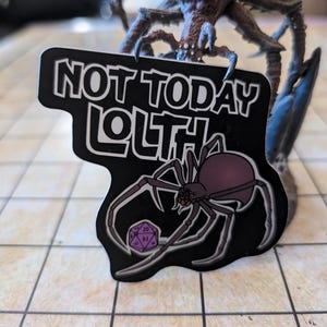 Puede incluir: Una pegatina en blanco y negro con una araña y el texto "Not Today Lolth". La araña sostiene un dado de 20 caras morado.