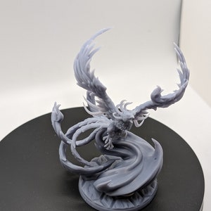 May include: A gray 3D printed miniature of a phoenix with its wings spread wide. The phoenix is standing on a circular base with a swirling design.