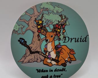 May include: A round sticker featuring a cartoon illustration of a deer with antlers decorated with leaves and mushrooms. The deer is holding a staff and is seated in front of a tree. The text "Druid" and "When in doubt, ask a tree" is printed on the sticker.