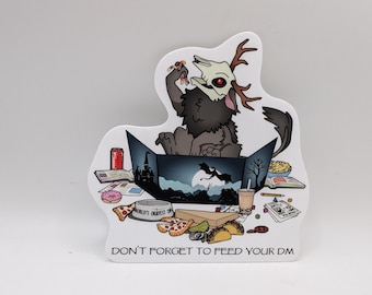 May include: A white sticker with a cartoon illustration of a black and grey creature with antlers, holding a pizza slice. The creature is sitting in a box with a dragon and a castle illustration. The sticker says "Don't forget to feed your DM".