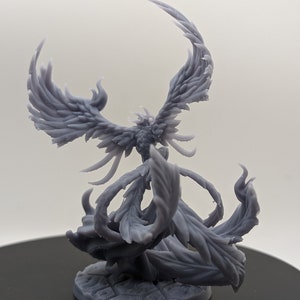 May include: A gray 3D printed miniature of a phoenix with its wings spread wide. The phoenix is standing on a circular base with a textured surface.
