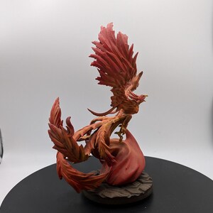 May include: A red and orange phoenix figurine with its wings spread wide. The phoenix is perched on a base of flames.