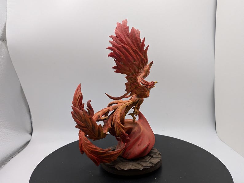 May include: A red and orange phoenix figurine with its wings spread wide. The phoenix is perched on a base of flames.