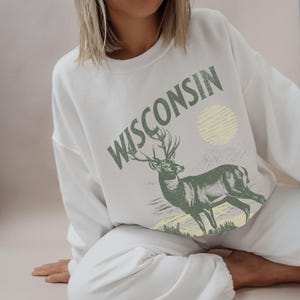 May include: White sweatshirt with a green deer and the word "WISCONSIN" printed on the front.