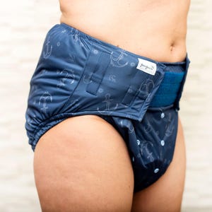 May include: A blue adult nappy with a white anchor print and a blue adjustable waistband. The nappy has the word "bumgenius" printed on the waistband.