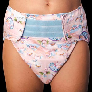 May include: A pink cloth nappy featuring a pattern of unicorns, rainbows, and clouds. The nappy has a light blue waistband and a snap closure. The brand name "pupus" is visible on the left side.