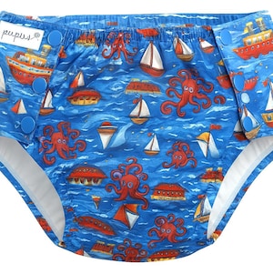 Puede incluir: Pañal de tela azul con temática náutica. El pañal presenta un estampado de barcos rojos, veleros y pulpos naranjas sobre un fondo azul. El pañal tiene cierres a presión azules y la marca "pupus" es visible.