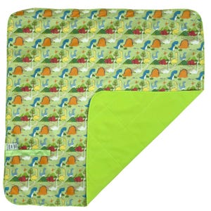 Puede incluir: Una alfombra de juego verde y amarilla con temática de dinosaurios con un reverso acolchado verde. La alfombra está doblada por la mitad, mostrando ambos lados.