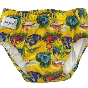 Peut inclure: Couche de bain jaune avec un imprimé coloré de dragons et de châteaux. La couche a une doublure intérieure blanche et le nom de la marque "pupus" est imprimé sur le devant.