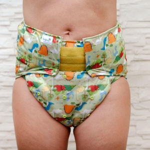 May include: A green, yellow, and blue reusable cloth diaper with a dinosaur print. The diaper has a yellow adjustable waistband and a snap closure.