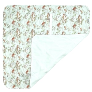 Peut inclure: Un tapis à langer vert clair avec une poche blanche. Le tapis présente un motif répétitif de cerfs bruns, de lapins et d'oiseaux dans un décor de forêt.