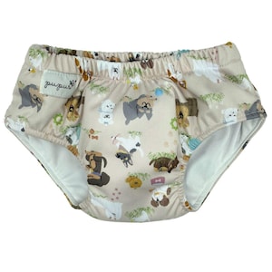 May include: Beige and white reusable training underwear with a print of various cartoon dogs. The underwear has a white elastic waistband and the text "puplush" is printed on the front.