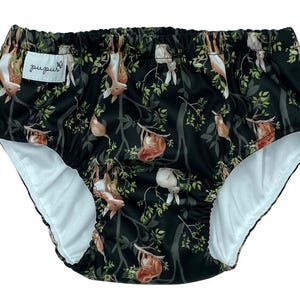 May include: Black and green reusable swim diaper with a white inner lining. The diaper has a print of deer and rabbits in a forest setting. The text "pupkus" is printed on the diaper.
