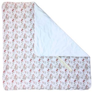 Puede incluir: Una manta rectangular con un patrón repetitivo de zorros rojos y follaje verde sobre un fondo blanco. La manta está parcialmente doblada para revelar un reverso acolchado de color blanco sólido e incluye una pequeña trabilla de tela blanca.