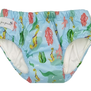 Peut inclure: Couche de bain bleue avec un imprimé de hippocampes et d'algues. La couche a une doublure blanche et le nom de la marque "pupus" est imprimé sur le côté.