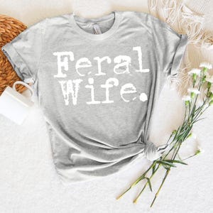 May include: Gray t-shirt with the text "Feral Wife" printed in white.