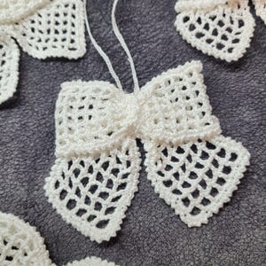 May include: White crocheted bow with a delicate, intricate pattern. The bow is tied with a loop and is ready to be hung as a decorative element.