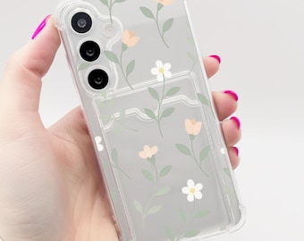 May include: A clear phone case with a floral design. The case has a built-in card holder and features a white background with pink and green flowers.
