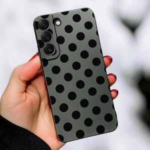 May include: A gray smartphone case featuring a repeating pattern of solid black polka dots. The case includes a rectangular camera cutout in the upper left corner, designed to accommodate a triple-lens camera system and a small circular flash.
