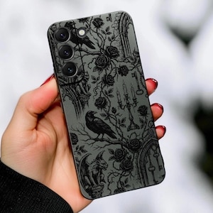 May include: A smartphone case featuring a dark grey background with a detailed black illustration of roses, a raven, a gargoyle, a candelabra, and architectural arches. The design covers the entire back of the phone, including the camera lens area.