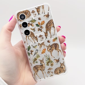 May include: A clear smartphone case featuring a repeating pattern of brown spotted fawns, small woodland birds, acorns, oak leaves, and mushrooms. The case has cutouts for a triple camera lens array on the upper left side and a transparent finish.