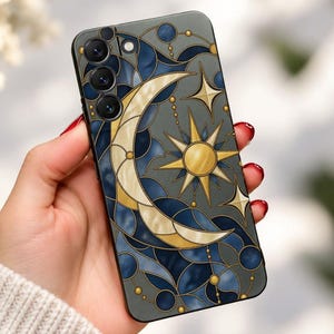 May include: A smartphone case featuring a stained glass style design with a crescent moon and a sun at the center. The pattern includes deep blue and grey segments outlined in gold, accented with small gold circles and four-pointed star shapes.