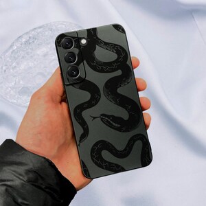May include: A black phone case with a snake pattern design. The case has a camera cutout and a black background.