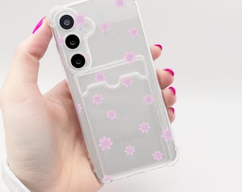 May include: A clear phone case with a pink floral pattern and a built-in card holder.