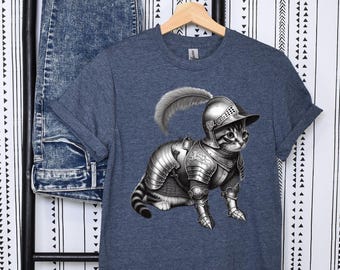 May include: A navy blue t-shirt featuring a detailed illustration of a cat in medieval armor, complete with a helmet and plume. The cat is depicted in a realistic style, with intricate details on the armor. The shirt is displayed on a wooden hanger.