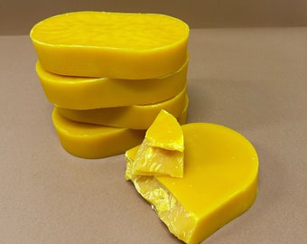 May include: A stack of four yellow beeswax blocks, with one block broken into two pieces. The beeswax is a natural product used for making candles, cosmetics, and other crafts.