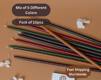 May include: A pack of 10 long, thin candles in a mix of 5 colours: brown, black, red, green, and tan. The candles are arranged in a fan shape on a brown surface. The text "Mix of 5 Different Colours" and "Pack of 10pcs" is visible in the image.