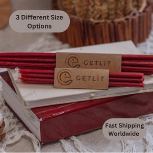 Puede incluir: Tres velas de cera de abeja roja apiladas una encima de la otra, con una etiqueta de papel marrón que dice "GETLIT" a cada lado. Las velas están encima de dos libros, uno blanco y otro rojo.