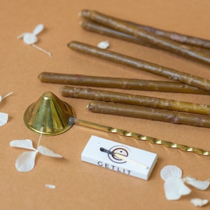 Op de afbeelding: Een set bruine tapers met een messing kaarsdover en een doosje lucifers met het opschrift "GETLIT".