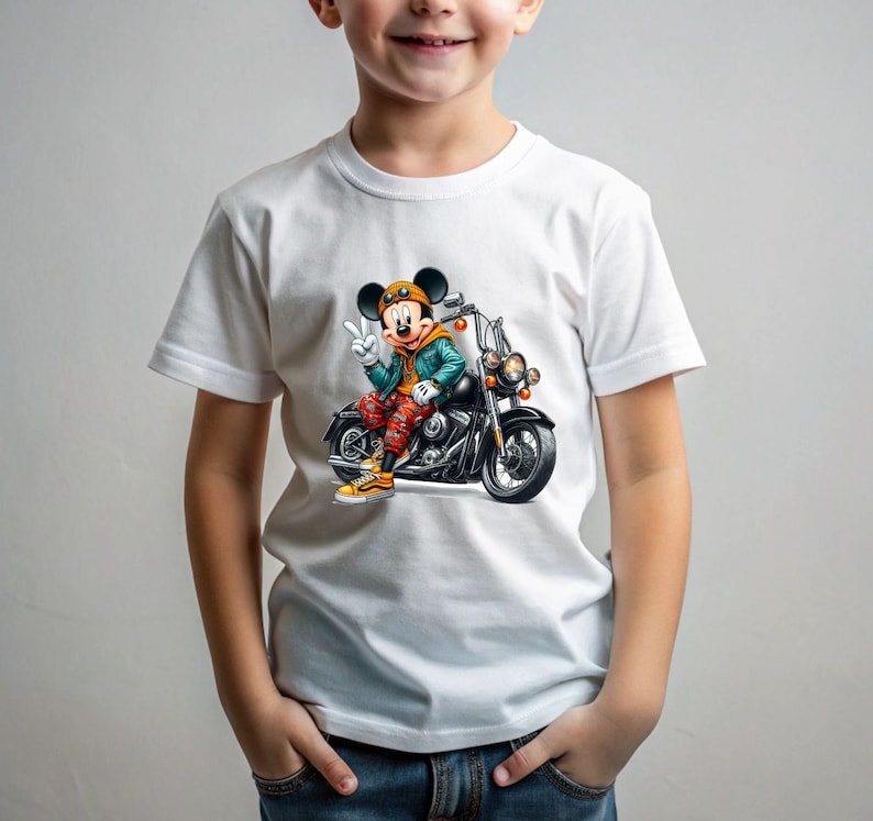 May include: White t-shirt with a graphic of Mickey Mouse riding a motorcycle. Mickey is wearing a blue jacket, red pants, and a yellow helmet. The motorcycle is black with chrome accents.