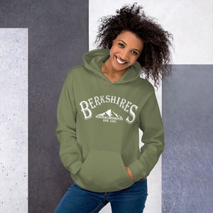 Könnte beinhalten: Ein grüner Kapuzenpullover mit einem weißen Grafikdruck, auf dem "Berkshires Massachusetts Est. 1761" mit einem Bergpanorama steht.
