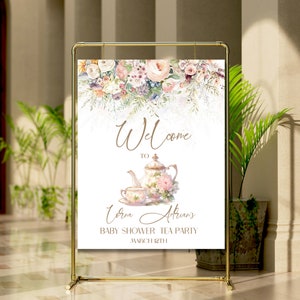 Op de afbeelding: Een welkomstbord voor een baby shower theepartij met een aquarel bloemenontwerp. Het bord toont een theepot en een theekopje met een bloemenpatroon. De tekst luidt "Welkom bij [Name]'s Baby Shower Tea Party op 8 maart".
