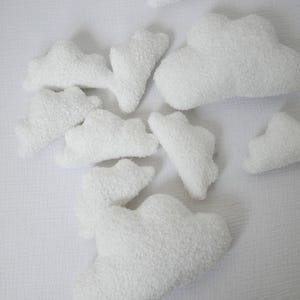 Puede incluir: Un conjunto de almohadas blancas y esponjosas con forma de nube. Las almohadas están dispuestas sobre una sábana blanca.