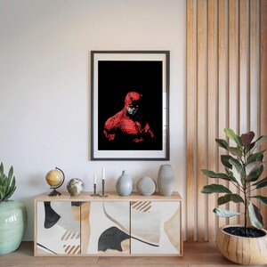 Pu&ograve; includere: Stampa artistica incorniciata con un'illustrazione rossa e nera di un supereroe. L'opera d'arte &egrave; appesa a una parete bianca sopra un mobile in legno con oggetti decorativi. Sono visibili anche una pianta in vaso e un mappamondo.