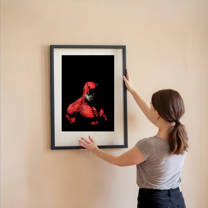 Pu&ograve; includere: Una stampa artistica incorniciata con un'illustrazione rossa e nera di un supereroe. L'opera raffigura un personaggio con un costume rosso e corna su sfondo nero. La stampa &egrave; in una cornice nera.