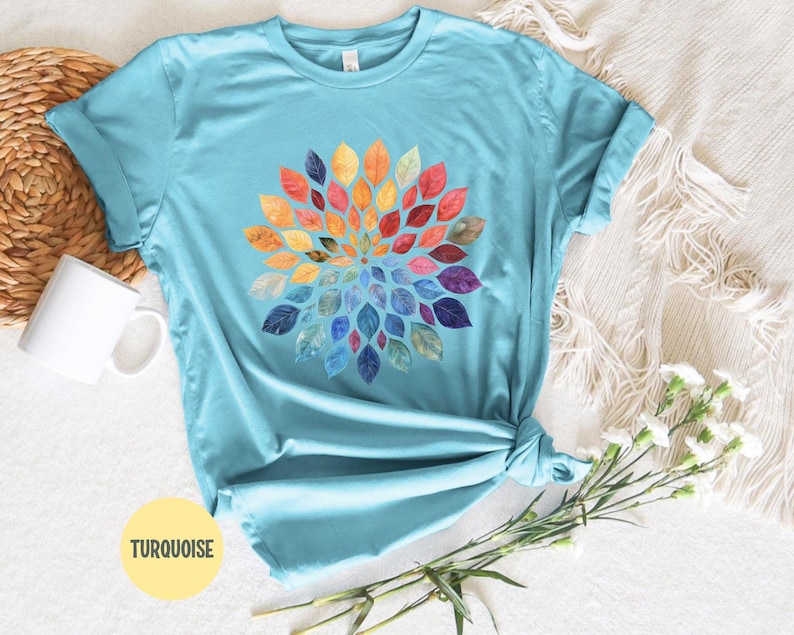 K&ouml;nnte beinhalten: Ein t&uuml;rkisfarbenes T-Shirt mit kurzen &Auml;rmeln und einer kreisf&ouml;rmigen Mandala-Grafik, die aus zahlreichen kleinen Bl&auml;ttern in einem Farbverlauf aus Rot, Orange, Gelb, Gr&uuml;n, Blau und Violett besteht. Das Shirt hat einen klassischen Rundhalsausschnitt.