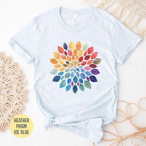 K&ouml;nnte beinhalten: Ein eisblaues, meliertes T-Shirt mit einer zentralen kreisf&ouml;rmigen Grafik aus aquarellartigen Bl&auml;ttern, die in einem lebendigen Regenbogenspektrum angeordnet sind und von einem kleinen Mittelpunkt aus strahlenf&ouml;rmig verlaufen.