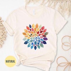 K&ouml;nnte beinhalten: Ein cremefarbenes Kurzarm-T-Shirt mit einer kreisf&ouml;rmigen Mandala-Grafik, die aus aquarellartigen Bl&auml;ttern in einem Farbspektrum aus Rot, Orange, Gelb, Gr&uuml;n, Blau und Violett besteht, welche in einem radialen Muster angeordnet sind.